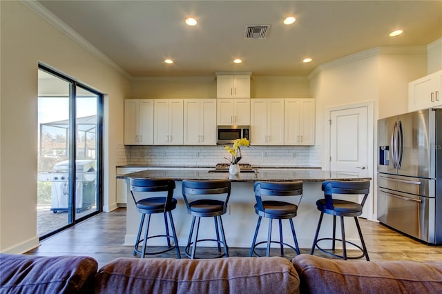 kitchen featuring a kitchen island with sink, visible vents, white cabinetry, appliances with stainless steel finishes, and dark stone countertops