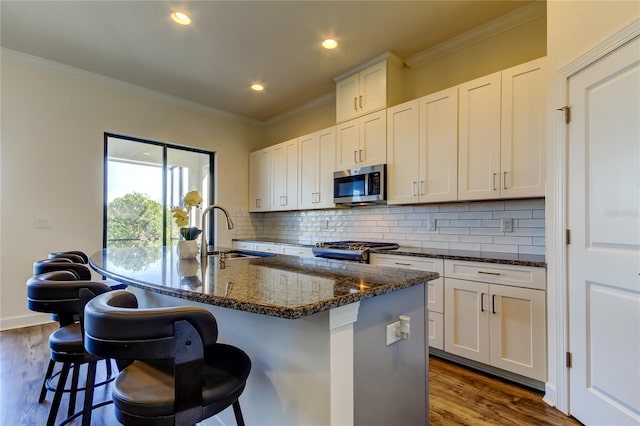 kitchen featuring stainless steel microwave, white cabinets, a sink, dark stone countertops, and an island with sink