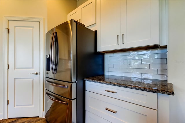 kitchen with tasteful backsplash, stainless steel fridge, white cabinets, and dark stone countertops