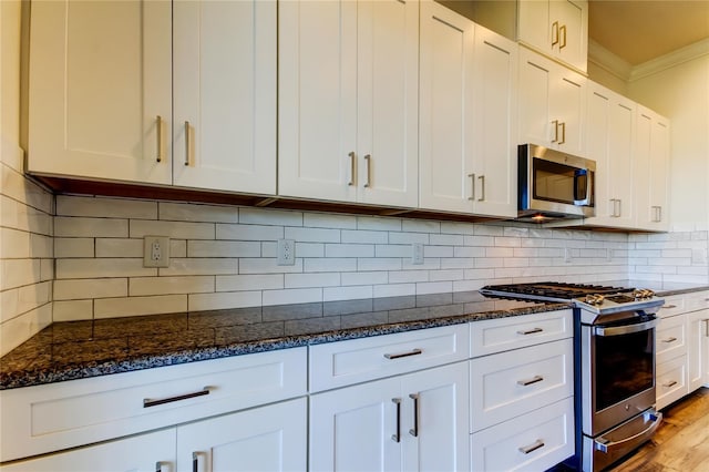 kitchen with dark stone counters, stainless steel appliances, ornamental molding, and white cabinets