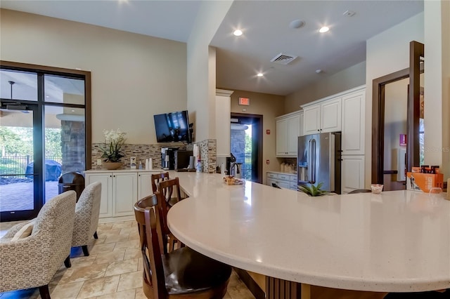 kitchen featuring a peninsula, stainless steel fridge, white cabinetry, and light countertops