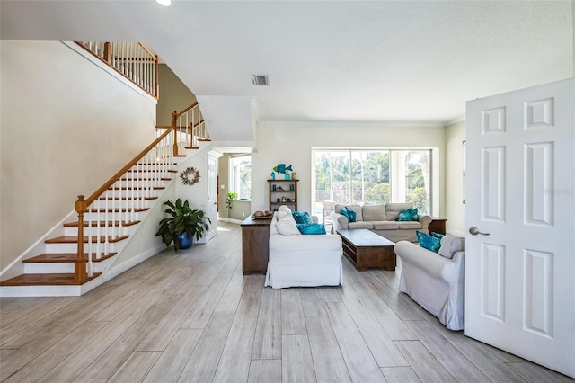 living room with wood finish floors, visible vents, baseboards, ornamental molding, and stairway