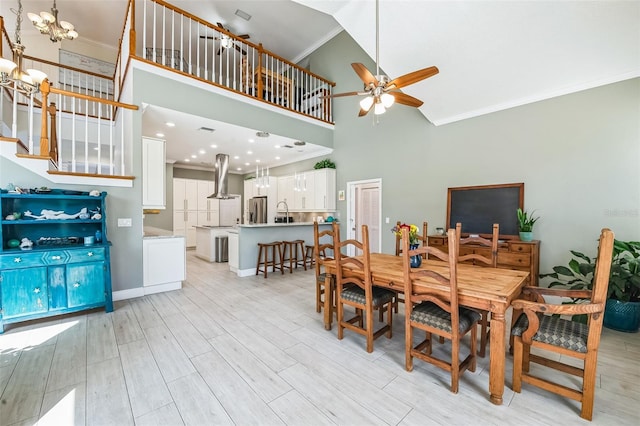 dining room with stairway, a high ceiling, ornamental molding, light wood-style floors, and ceiling fan with notable chandelier