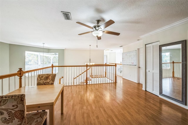 interior space featuring visible vents, ornamental molding, wood finished floors, a textured ceiling, and an upstairs landing