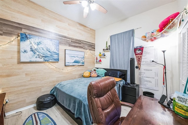 bedroom with ceiling fan, wooden walls, and wood finished floors