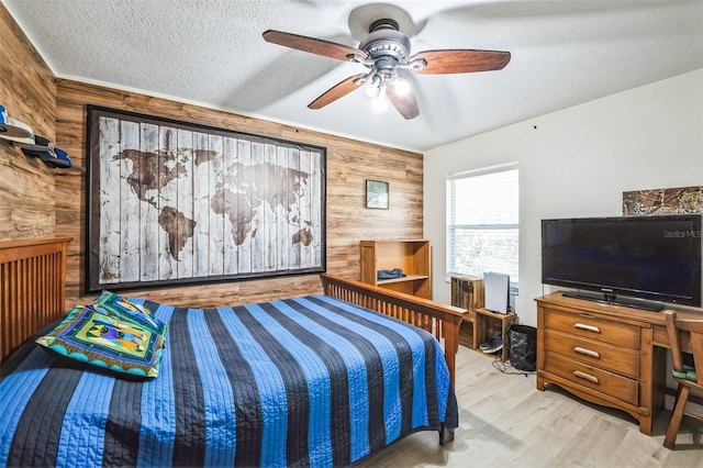 bedroom with a textured ceiling, ceiling fan, wood finished floors, and wooden walls