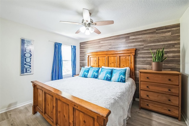 bedroom with a ceiling fan, baseboards, a textured ceiling, and light wood finished floors