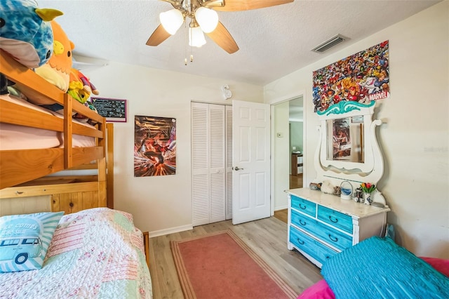 bedroom featuring a textured ceiling, ceiling fan, light wood-style flooring, visible vents, and a closet