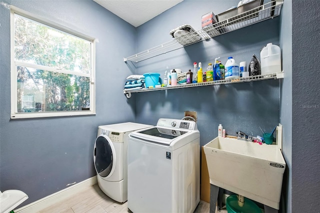 laundry area featuring laundry area, a sink, baseboards, light wood-type flooring, and washer and clothes dryer