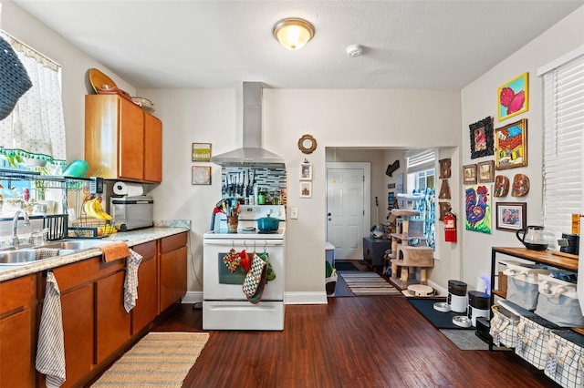 kitchen with dark wood-style floors, electric stove, light countertops, brown cabinetry, and wall chimney exhaust hood