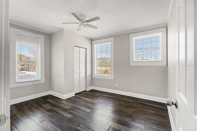 unfurnished bedroom featuring dark wood-style flooring, multiple windows, crown molding, and baseboards