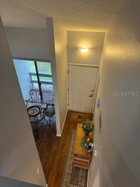 doorway to outside featuring a textured ceiling, dark wood finished floors, and baseboards