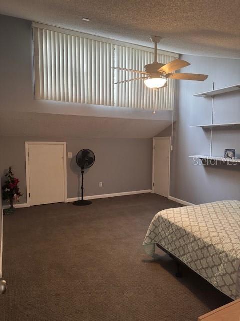 unfurnished bedroom featuring a textured ceiling, ceiling fan, baseboards, vaulted ceiling, and dark carpet