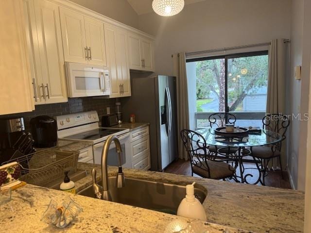 kitchen with white appliances, lofted ceiling, light stone counters, white cabinetry, and a sink