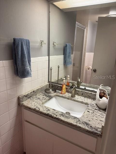 full bathroom with a shower stall, tile walls, and vanity