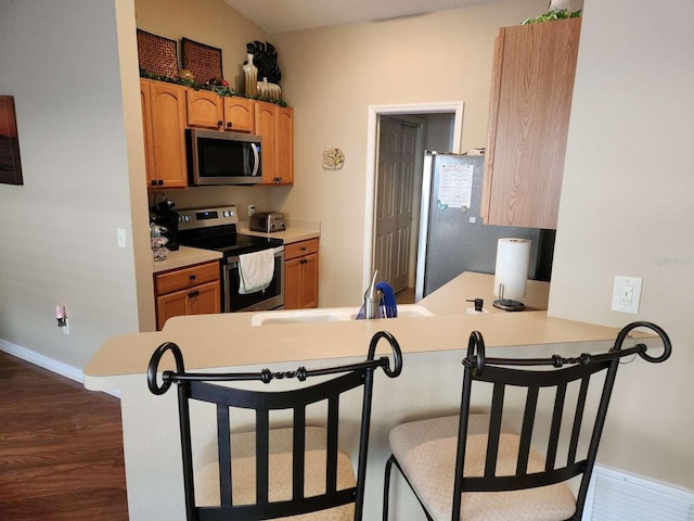 kitchen featuring dark wood-style floors, appliances with stainless steel finishes, a peninsula, light countertops, and a sink