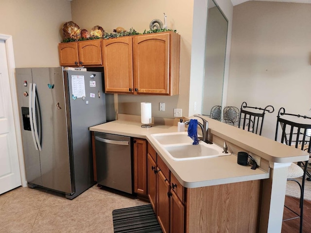 kitchen with a peninsula, a sink, light countertops, appliances with stainless steel finishes, and brown cabinets