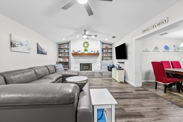 living room with built in features, wood finished floors, a large fireplace, ceiling fan, and vaulted ceiling