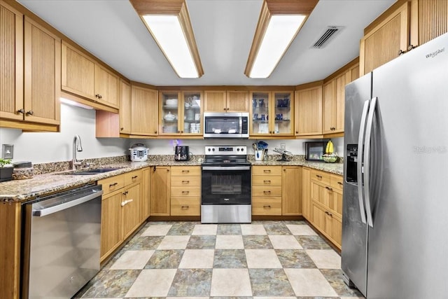 kitchen featuring light stone countertops, visible vents, a sink, stainless steel appliances, and glass insert cabinets