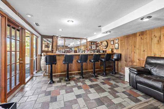 bar featuring visible vents, wood walls, a textured ceiling, and wet bar