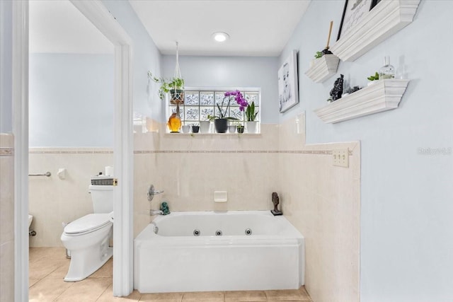 bathroom featuring toilet, wainscoting, tile patterned floors, a tub with jets, and tile walls