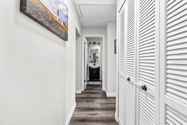 corridor featuring dark wood-style floors, baseboards, and a sink