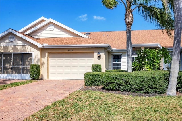 ranch-style home featuring decorative driveway, roof with shingles, an attached garage, and stucco siding