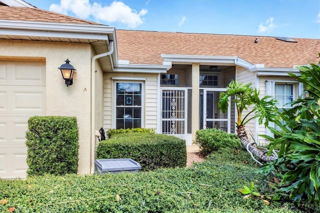 entrance to property featuring roof with shingles, an attached garage, and stucco siding