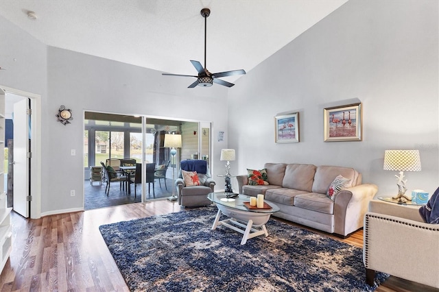 living room with ceiling fan, wood finished floors, a towering ceiling, and baseboards