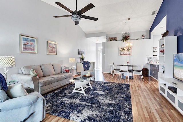 living room featuring baseboards, high vaulted ceiling, wood finished floors, and ceiling fan with notable chandelier