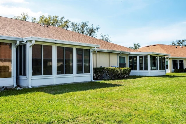 back of house featuring a yard, roof with shingles, and a sunroom