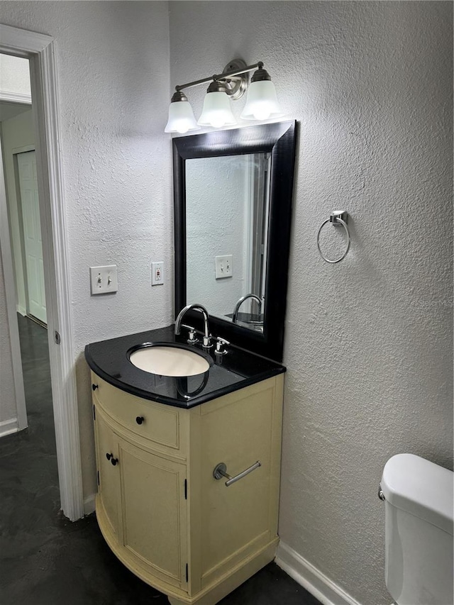 half bathroom with baseboards, a textured wall, vanity, and toilet