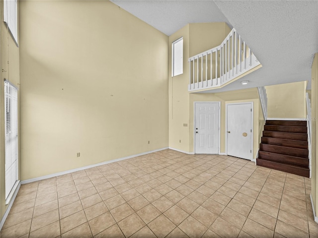 unfurnished living room featuring baseboards, a high ceiling, stairway, and tile patterned flooring