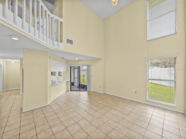 empty room with a high ceiling, visible vents, baseboards, and light tile patterned flooring