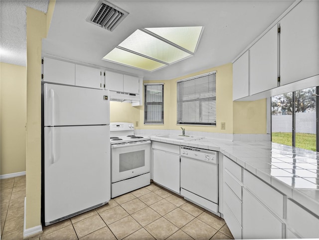 kitchen with under cabinet range hood, white appliances, a sink, visible vents, and tile counters