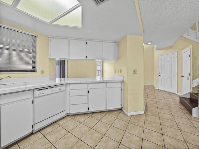 kitchen with tile countertops, light tile patterned floors, a sink, white cabinetry, and dishwasher