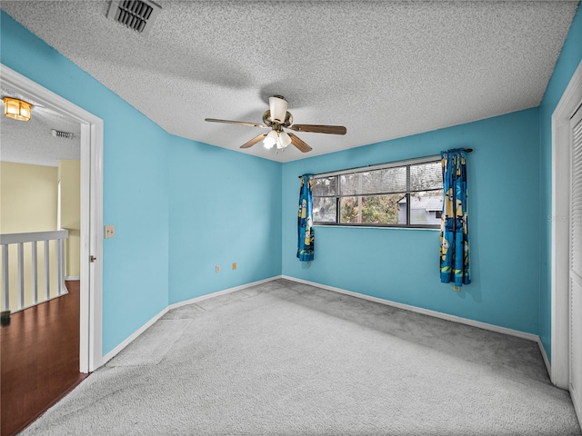 carpeted spare room with baseboards, a textured ceiling, visible vents, and a ceiling fan