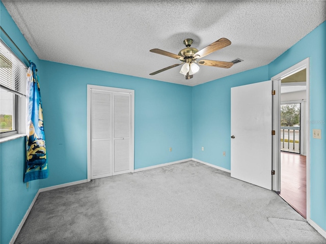 unfurnished bedroom featuring a textured ceiling, ceiling fan, carpet flooring, visible vents, and a closet