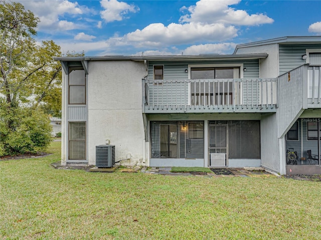 rear view of property with central AC unit, a lawn, a balcony, a sunroom, and stucco siding