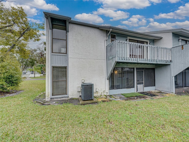 back of house with stucco siding, a lawn, and central AC unit