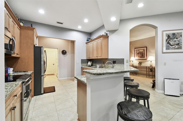 kitchen featuring appliances with stainless steel finishes, visible vents, a kitchen bar, and light stone countertops