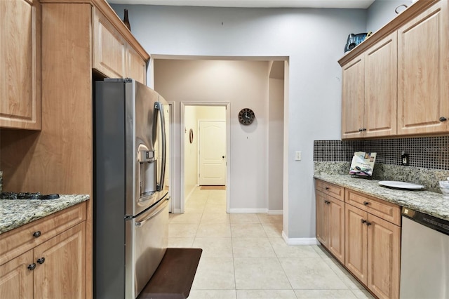 kitchen with light stone counters, light tile patterned floors, tasteful backsplash, appliances with stainless steel finishes, and baseboards