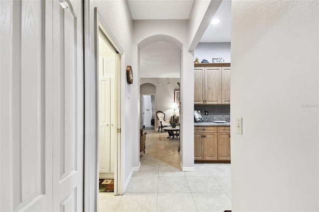 hall with baseboards, arched walkways, and light tile patterned flooring