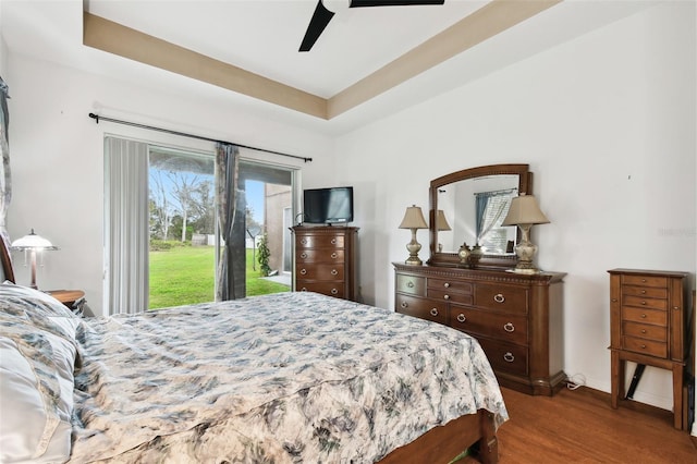 bedroom featuring a ceiling fan, access to outside, a tray ceiling, and dark wood-style flooring