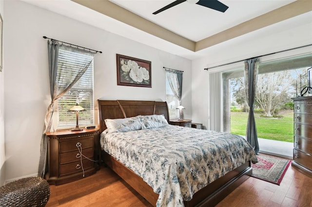 bedroom with a tray ceiling, access to outside, a ceiling fan, and dark wood-style flooring