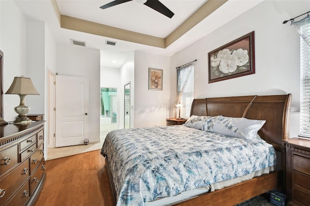 bedroom with a raised ceiling, visible vents, and ensuite bath