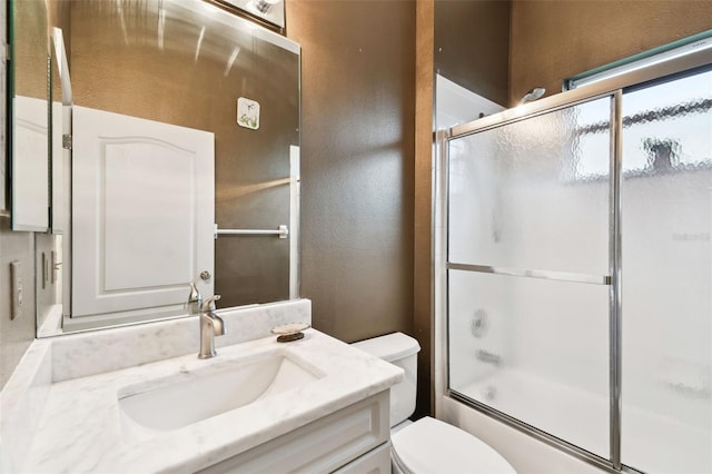 bathroom featuring toilet, a textured wall, combined bath / shower with glass door, and vanity