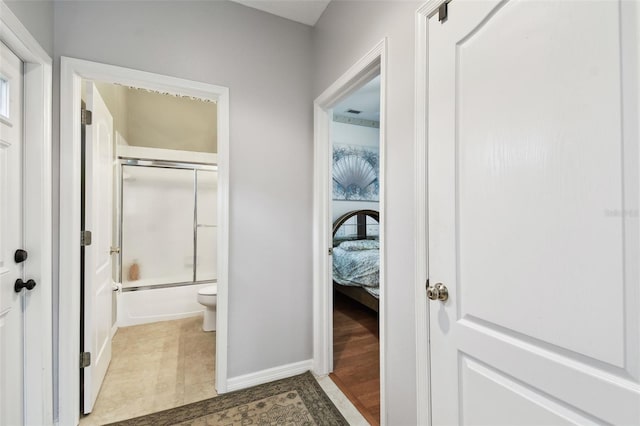 bathroom featuring toilet, baseboards, and bath / shower combo with glass door