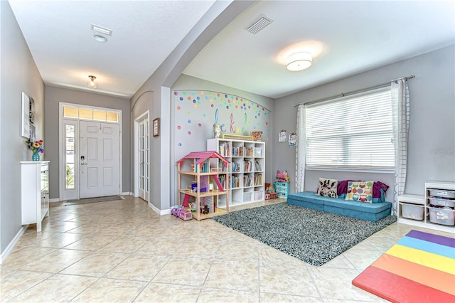 recreation room with baseboards, tile patterned floors, visible vents, and a healthy amount of sunlight