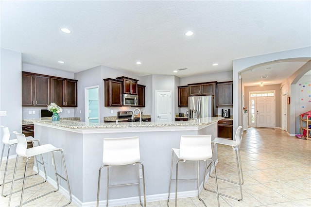 kitchen featuring arched walkways, stainless steel appliances, a spacious island, dark brown cabinetry, and a sink